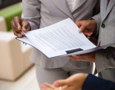 Diverse business partners reading contract together. Business man and woman wearing formal suits, standing and holding open folder with document. Agreement concept